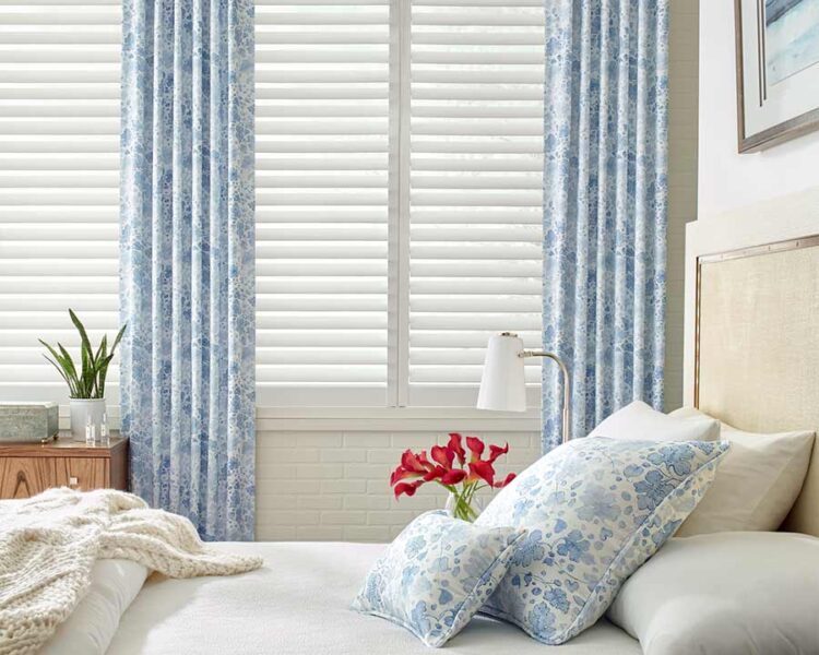 coastal guest bedroom white plantation shutters framed by blue floral curtains in maple grove, mn