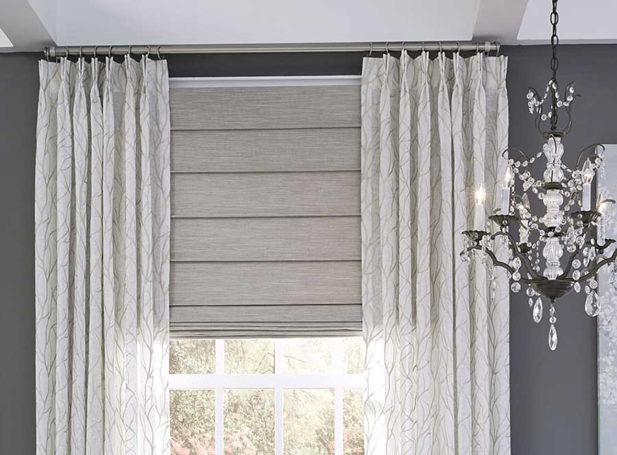 custom drapery paired with shades in a dark gray room with a chandelier